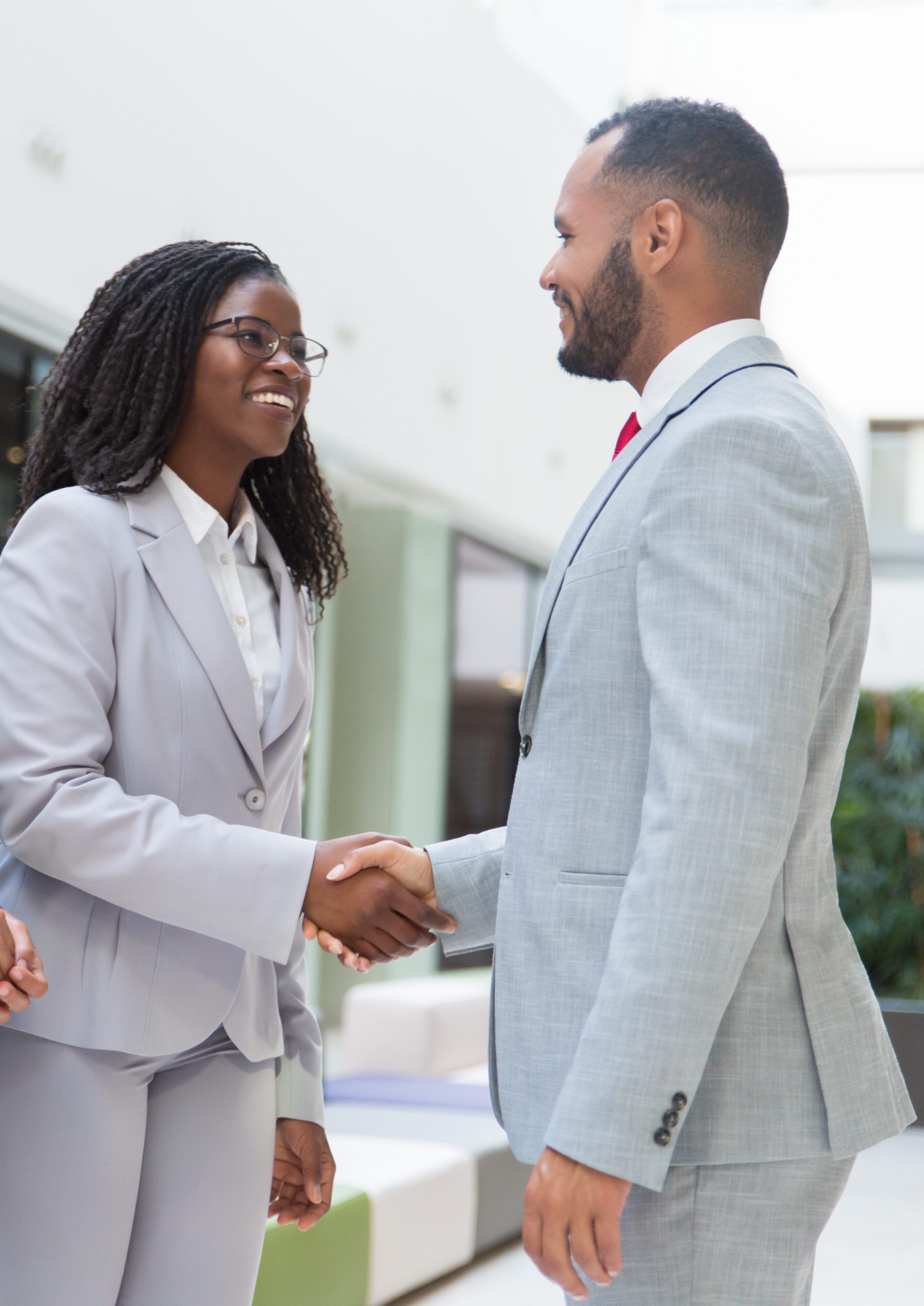 Happy joyful diverse business partners greeting each other in hallway. Business man and women standing, shaking hands with each other, talking and smiling. Successful partnership concept